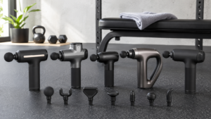 Five massage guns and attachment heads arranged in a modern home gym